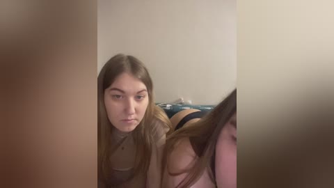 Video of a young woman with long brown hair, wearing a brown top, lying on a bed with a blue blanket, in a dimly lit room.