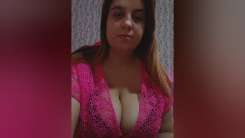 Video of a plus-sized woman with fair skin, brown hair, and large breasts, wearing a pink lace top, against a floral-patterned background.