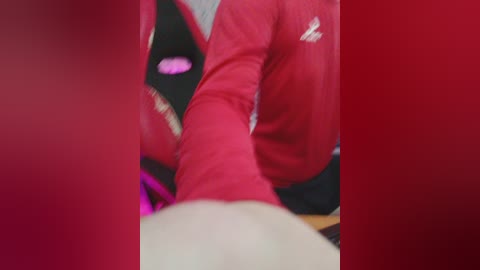 A close-up video of a person wearing a red and black athletic jacket, with a blurred background, focusing on the sleeve and arm. The image has a red tint, emphasizing the jacket's vibrant color.
