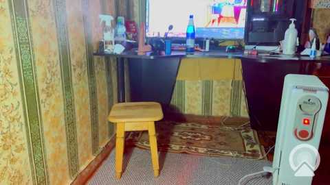 Video of a cluttered, vintage-style room with green and yellow patterned wallpaper, a wooden stool, a TV showing a colorful cartoon, and a space heater.