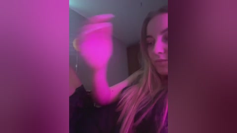 Media: Video of a young woman with long, blonde hair, wearing a black top, captured in a dimly-lit room with purple lighting.