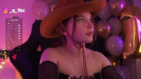 Video of a young woman with fair skin and brown hair, wearing a large brown hat, black off-shoulder top, and headphones, seated in a gaming chair amidst a room filled with balloons and glowing lights.