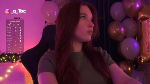 A video of a young woman with long, wavy auburn hair, wearing a green top, sitting in a dark room adorned with golden balloons and fairy lights.