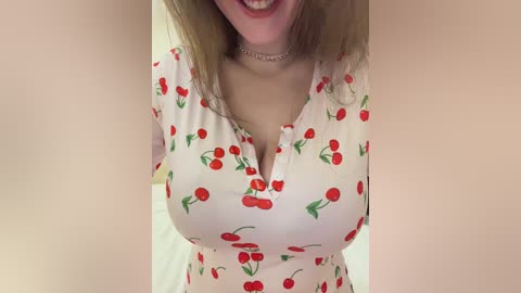 Media: Video of a smiling woman with light skin and long blonde hair, wearing a white dress adorned with cherry patterns and a thin choker necklace.