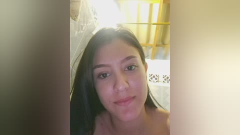 Video of a young woman with long black hair, fair skin, and a neutral expression, standing in a dimly lit, rustic bathroom with wooden beams and a tiled wall.