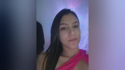 Video of a young Asian woman with long, straight black hair, wearing a pink off-shoulder top, smiling. Background is blurry, with purple and blue lighting effects.
