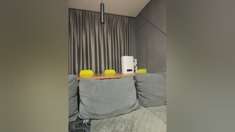 Video of a minimalist, modern room with grey walls, light grey carpet, and a wooden table with a white teapot and four bright yellow chairs.