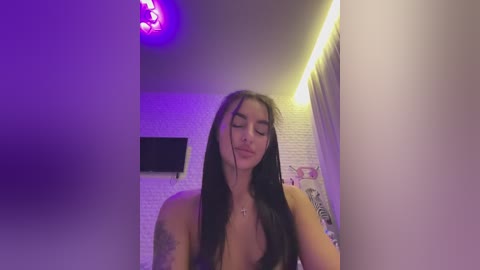 Media: A video of a young woman with long black hair, medium build, wearing a black top, standing in a dimly lit room with purple and yellow lighting, visible tattoos on her arms.