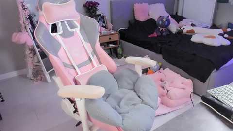 Video of a pink and grey gaming chair with a plush blanket, set in a cozy, cluttered bedroom with a bed, stuffed animals, and a laptop.