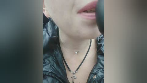 Video of a close-up, partially obscured face with a black leather jacket and necklace, wearing a black mask, possibly taken in a dimly lit environment.