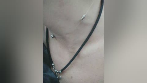 Video of a close-up of a person's neck adorned with a delicate, black leather necklace featuring small, silver charms. The skin is light-toned, with visible veins and a soft, smooth texture. The background is blurred, focusing attention on the jewelry.
