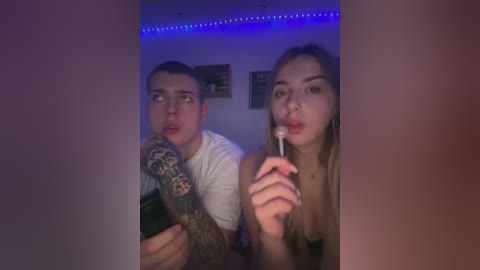 Media: A video of two young adults, a man with tattoos and a woman with blonde hair, in a dimly lit room, both holding toothbrushes, smiling.