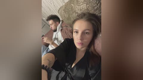 Media: Video of a young couple sitting on a couch; man in a hoodie, woman in a black robe, both absorbed in smartphones.