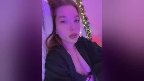 Video of a fair-skinned woman with red hair, wearing a black robe, lying on a bed with a purple light.