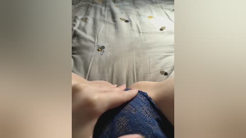 Media: A video shows a person\u2019s legs and hand, wearing blue shorts, lying on a bed with a patterned beige sheet featuring small bees. The scene appears intimate and casual.