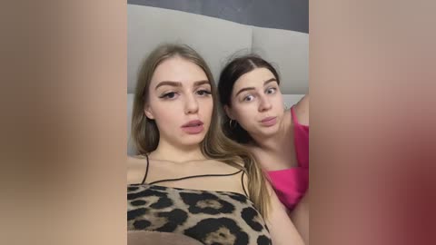 Media: Video of two young women with fair skin, long hair, and light makeup, one in a leopard print top, the other in a pink tank top, sharing a playful moment in a casual setting.