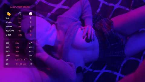 Video of a nude woman with fair skin, lying on a grid-patterned bed, under a purple light, displaying a smartphone screen showing time, temperature, and location.