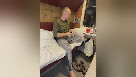 Media: A video shows a bald, middle-aged man in a green shirt and camouflage pants sitting on a bunk bed in a train compartment, focused on a phone, surrounded by personal items and a pair of shoes.