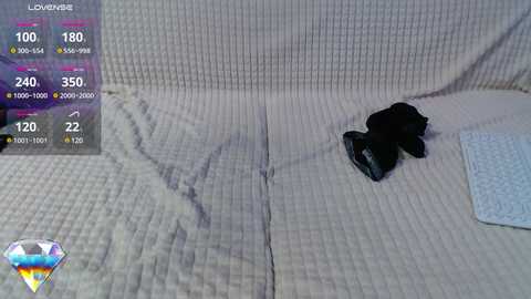 Video of a cream-colored, quilted sofa with a black, wrinkled pillow and a blue-patterned throw pillow. A virtual weather overlay shows rain, temperature, and wind speed.