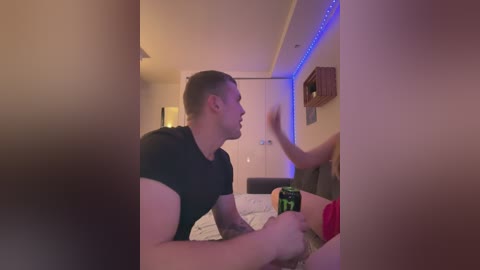 Media: Video of a muscular man in a black shirt, playing with a green can, in a dimly lit room with blue LED strip lighting and a wooden shelf.