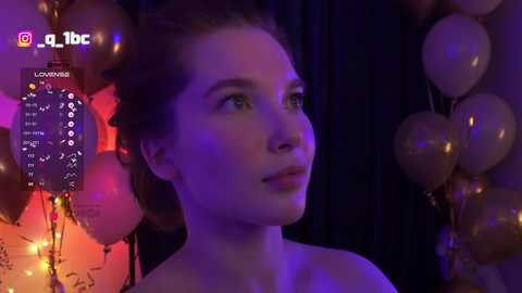 Video of a young Caucasian woman with fair skin and brown hair, illuminated by purple and orange lights, surrounded by gold balloons, looking contemplative.