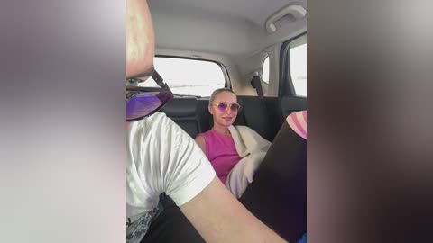 Video of a woman with sunglasses and a pink top in a car, looking relaxed.