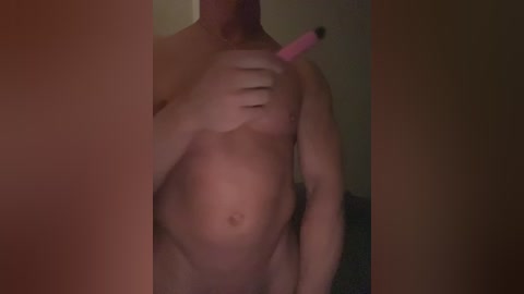 A video of a shirtless, light-skinned man with a toned abdomen holding a pink vibrator near his left nipple. The background is dark and blurry.