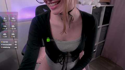 Media: A video of a smiling woman with glasses, wearing a black cardigan over a gray tank top, sitting at a desk in a dimly lit room with a virtual reality setup.