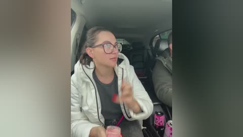 Media: A video of a woman with glasses and brown hair, wearing a white hoodie and gray t-shirt, holding a red straw in a car.