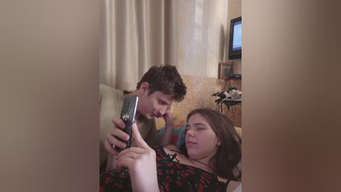 Video of a young Caucasian couple cuddling on a couch; man with short brown hair, woman with long brown hair, both wearing casual clothes, watching TV.