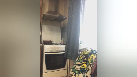 A video of a compact kitchen with a white stove, beige walls, and a colorful, patterned blanket draped over the back of a chair.