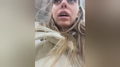Media: Video of a young Caucasian woman with long, blonde hair, wearing a beige sweater, taken from a low angle, showing her face and shoulders.