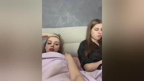 Media: Video of two young women in bed; one with blonde hair and a flushed face, the other with brown hair and a neutral expression.