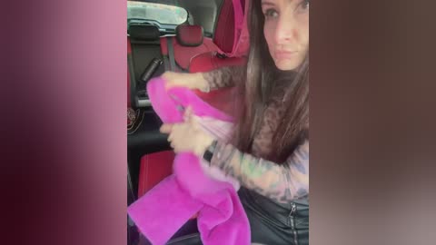 Media: A video captures a tattooed woman in a car, wearing a pink sweater, black pants, and a wristwatch, with a baby in a pink car seat in the background.