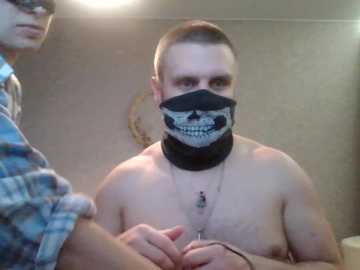 Video of a shirtless, muscular man with a black mask depicting a skull, wearing a black scarf, in a dimly lit room.