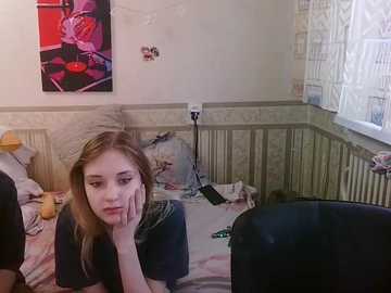 Media: A video of a young girl with long blonde hair, resting her head on her hand, in a cluttered, dimly-lit room with floral wallpaper and a baby crib.