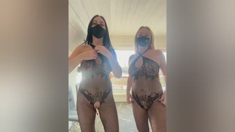 Media: Video of two women in black lace lingerie, fishnet stockings, and face masks, standing indoors with a wooden ceiling, one with a visible erection.