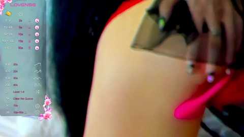 Media: Video of a close-up of a person's arm and hand holding a pink vibrator, with a blurred background featuring a digital screen displaying a pink and white interface.