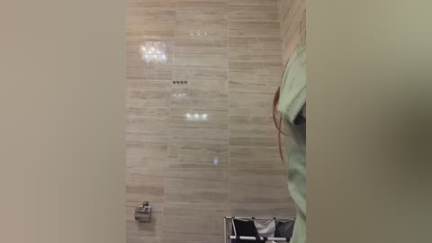 Video of a modern bathroom with beige tiled walls, a green towel hanging on a metal rack, and a toilet paper roll mounted on the left wall.