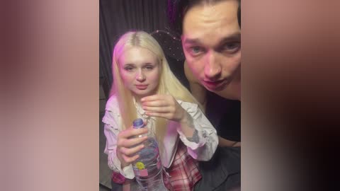 Video of a blonde woman in a white shirt and plaid skirt, holding a water bottle, standing beside a man with short hair in a black shirt. They are smiling.