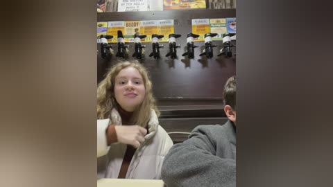 Media: Video of a blonde girl in a beige coat at a self-service beer tap wall in a dimly lit bar, surrounded by beer taps and posters.
