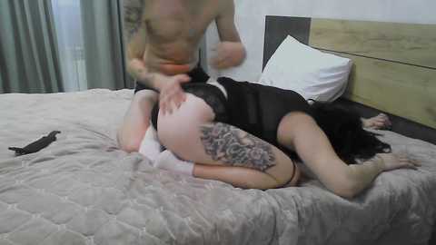 Video of a tattooed, shirtless man on a bed with a naked woman in leopard-print lingerie, her back arched, face obscured by a pillow.