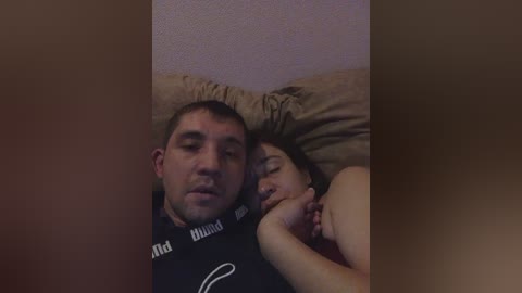 A video of a sleeping man and woman, both Caucasian, with the man in a black t-shirt and the woman in a red top, lying on beige pillows against a textured pink wall.