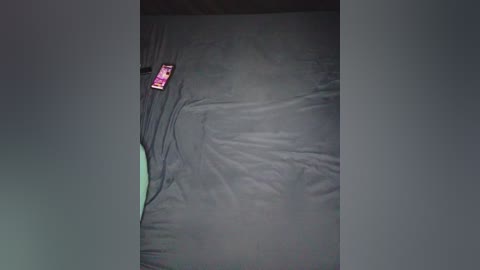 A video of a dark, rumpled bedsheet with a pink phone lying on it, partially visible at the bottom left corner. The scene is dimly lit, casting shadows and emphasizing the texture of the wrinkled fabric.