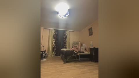 A video of a dimly lit bedroom with a ceiling light, beige walls, a bed with a person in underwear, and a cat in the corner.