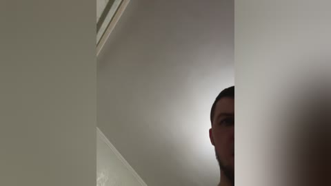 A video of a man's face partially obscured by a white curtain, with a beige wall in the background. The man has short, dark hair and a serious expression.