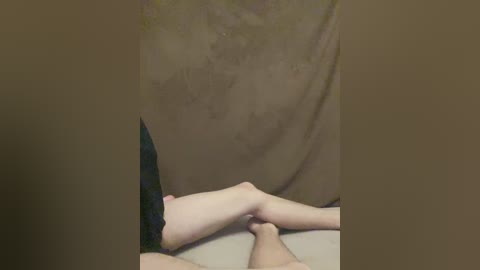 A video of a close-up of a man's legs and a woman's feet, with the woman's bare feet holding the man's hands. The background is blurred and dark, with a beige surface underneath.