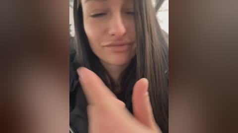 Media: Video of a young woman with long, straight brown hair, wearing a black shirt, and making a peace sign with her fingers, looking contemplative.