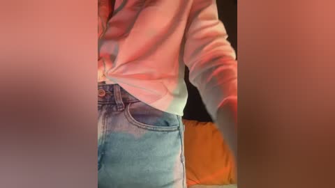 A video of a person wearing a white long-sleeve shirt tied at the waist and high-waisted blue jeans, with a red light casting a warm glow on the left side.
