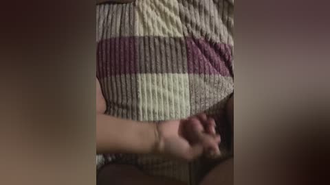 A close-up video of a person's clenched fist and a beige and purple striped sweater, with a blurred background. The texture of the sweater appears soft and knitted. The image is dimly lit.